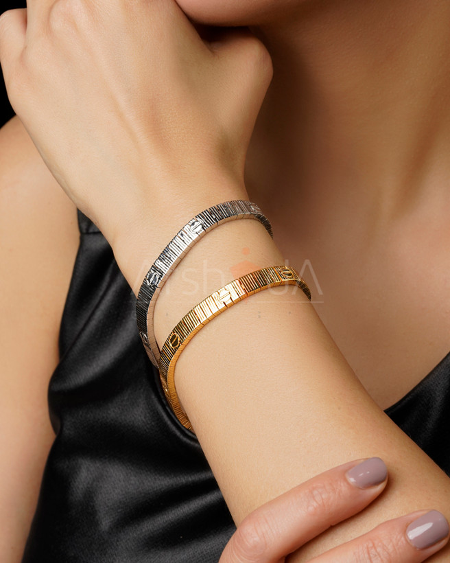 نمای نزدیک از دستبندهای لاو کارتیر رنگ طلایی و سفید با بافت خطی و نماد پیچ کارتیر بر روی دست مدل.