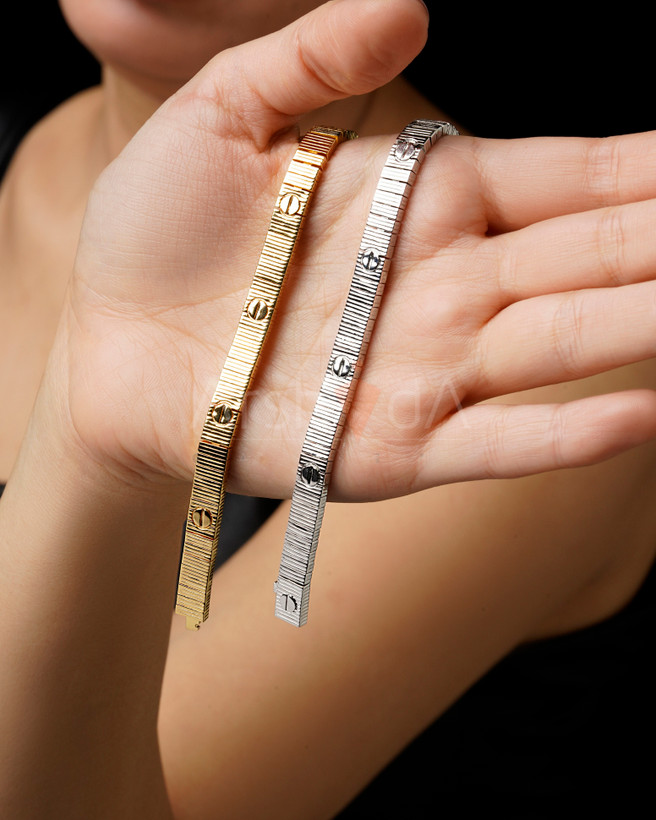 نمای نزدیک از دستبندهای لاو کارتیر رنگ طلایی و سفید با بافت خطی و نماد پیچ کارتیر بر روی دست مدل.